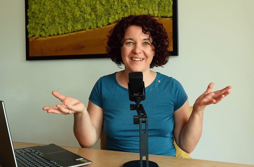 Paulina Hornbachner als Podcasterin - Paulina sitzt an einem Tisch, vor Ihr ein Podcast Mikrofon und gestikuliert beim Sprechen.